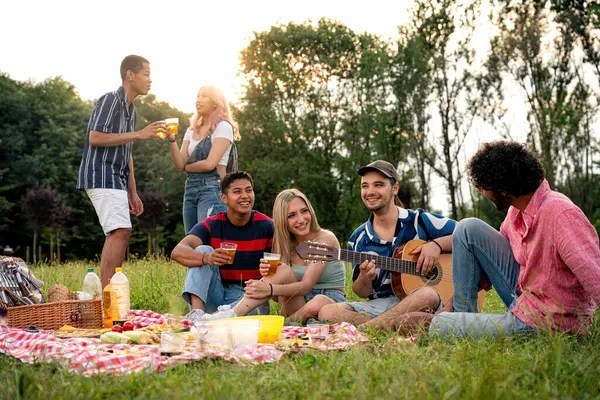 Friends enjoying a sunny picnic outdoors with drinks and snacks.