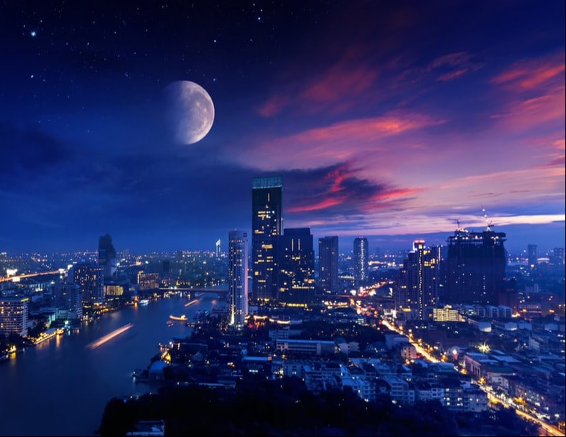 City skyline at dusk with a large moon above.