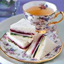 Elegant tea cup with layered finger sandwiches on matching floral plate.