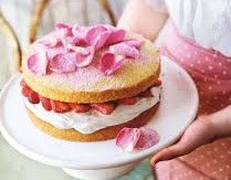 A small cake with strawberries and pink rose petals on top.