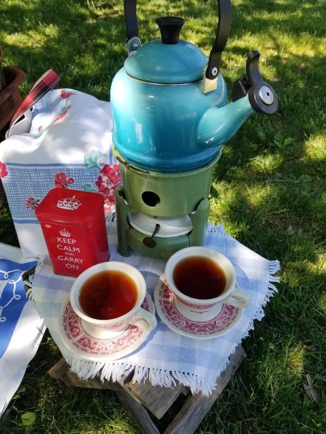 Traditional tea setup with a blue kettle, two cups of tea, and tea packaging outdoors.