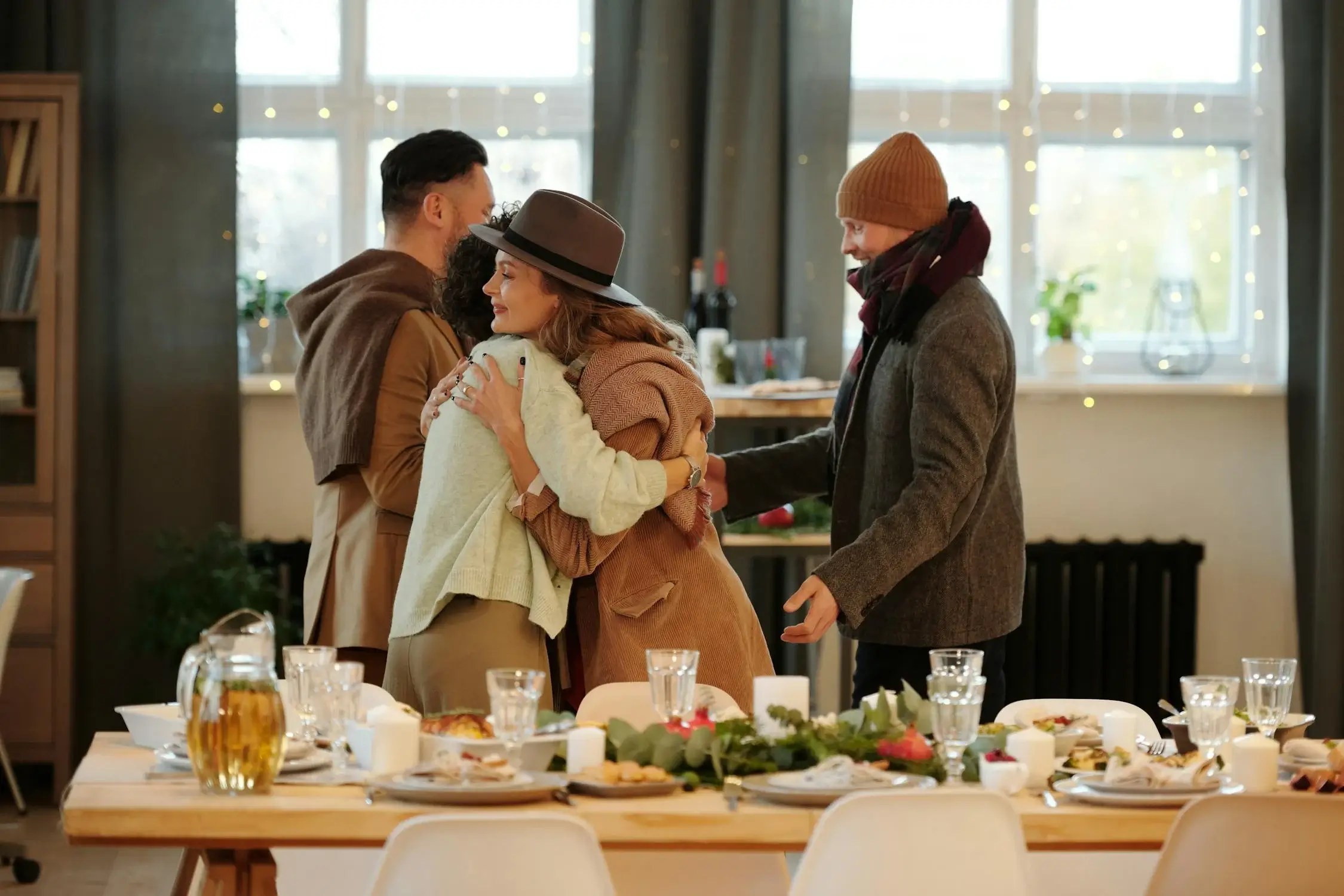 Two couples warmly embrace in a cozy, well-lit dining space.