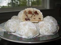 Powdered sugar-covered cookies with a fruit and nut filling on a plate.