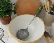 A white bowl with a strainer ladle inside on a kitchen counter.