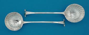Two identical silver spoons with decorative handles on a blue background.