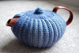 A teapot covered with a blue knitted cozy.
