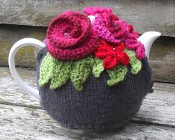 Hand-knitted cozy on a teapot with colorful flowers and leaves.