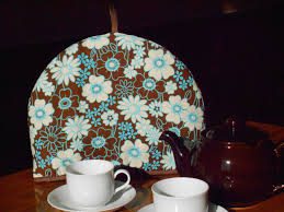 Tea set with floral-patterned cozy and white cups on a wooden table.