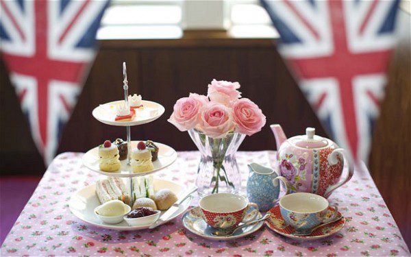 Elegant afternoon tea setup with floral teapot, pink roses, and assorted treats.