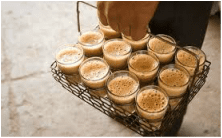 A tray of Indian chai served in glass cups with hands reaching in.