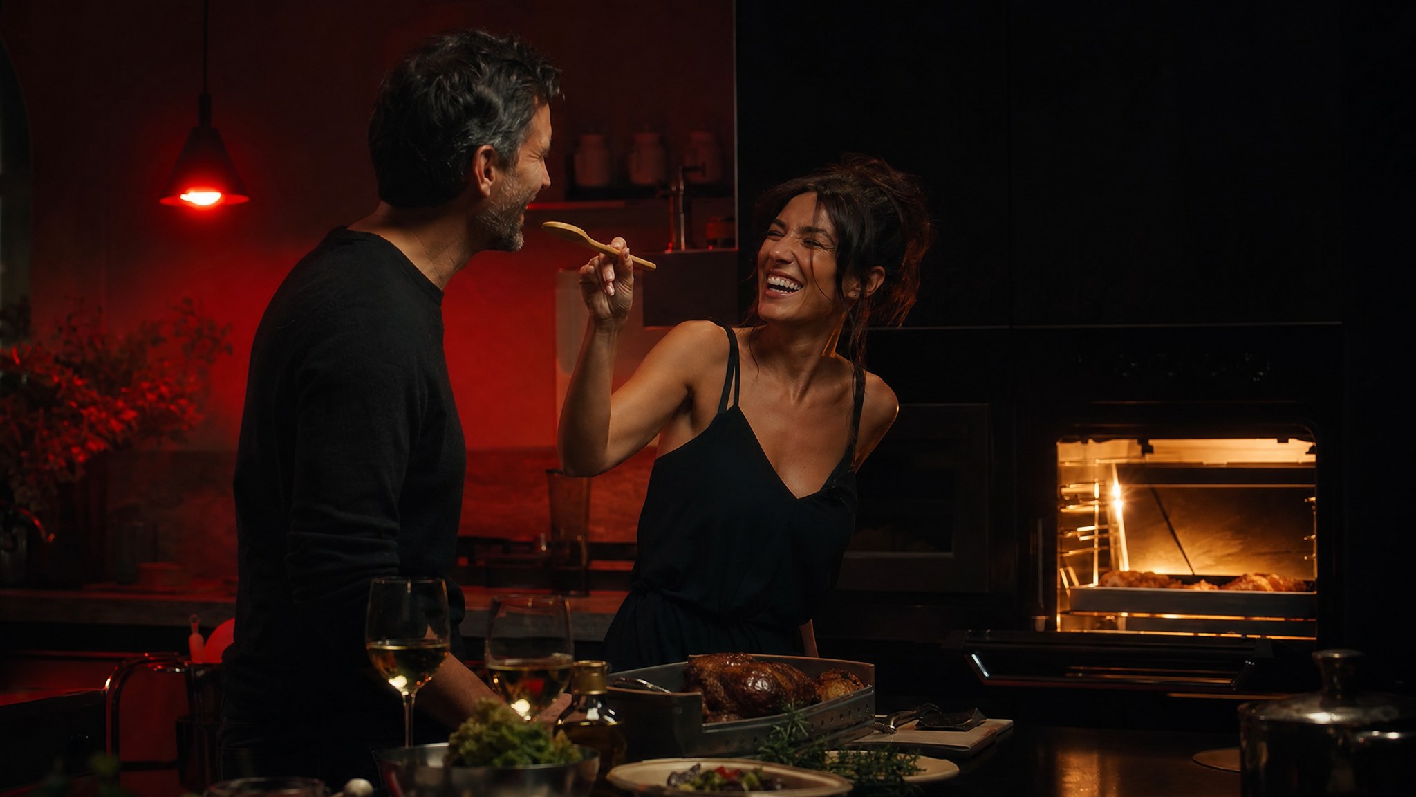 Couple laughing together while cooking at home by warm oven light