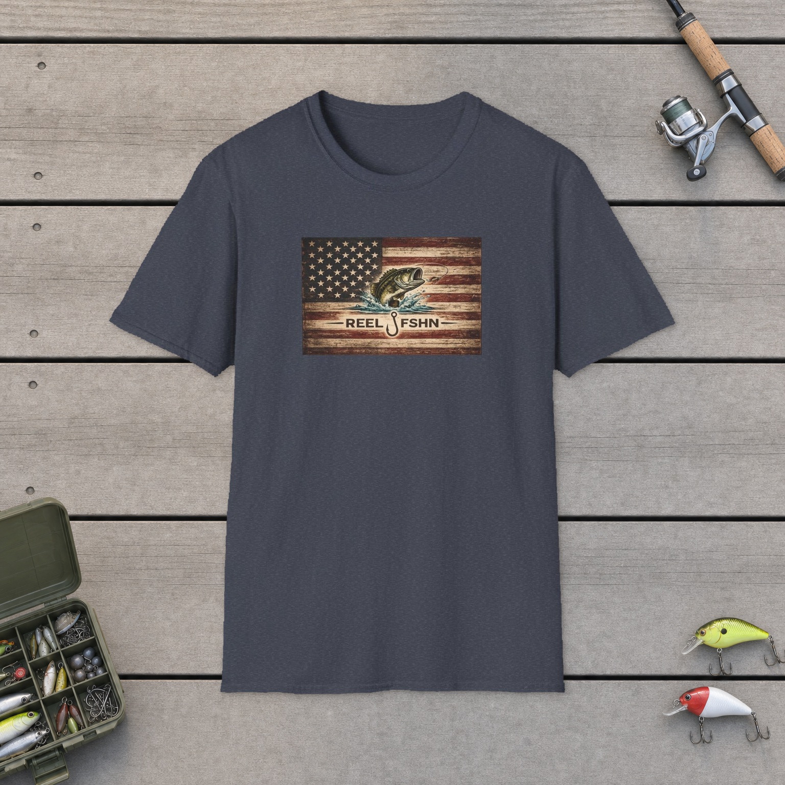 American Flag With Bass T-Shirt on a wooden dock with a fishing rod, reel, tackle box, and two lures