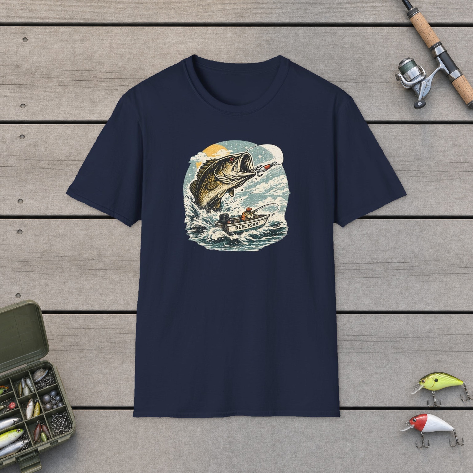 Bass Graphic with Boat T-Shirt on a wooden dock with a fishing rod, reel, tackle box, and two lures