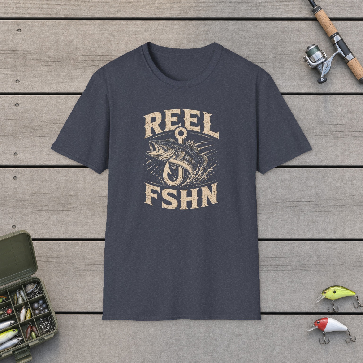 Bass Through Hook T-Shirt on a wooden dock with a fishing rod, reel, tackle box, and two lures