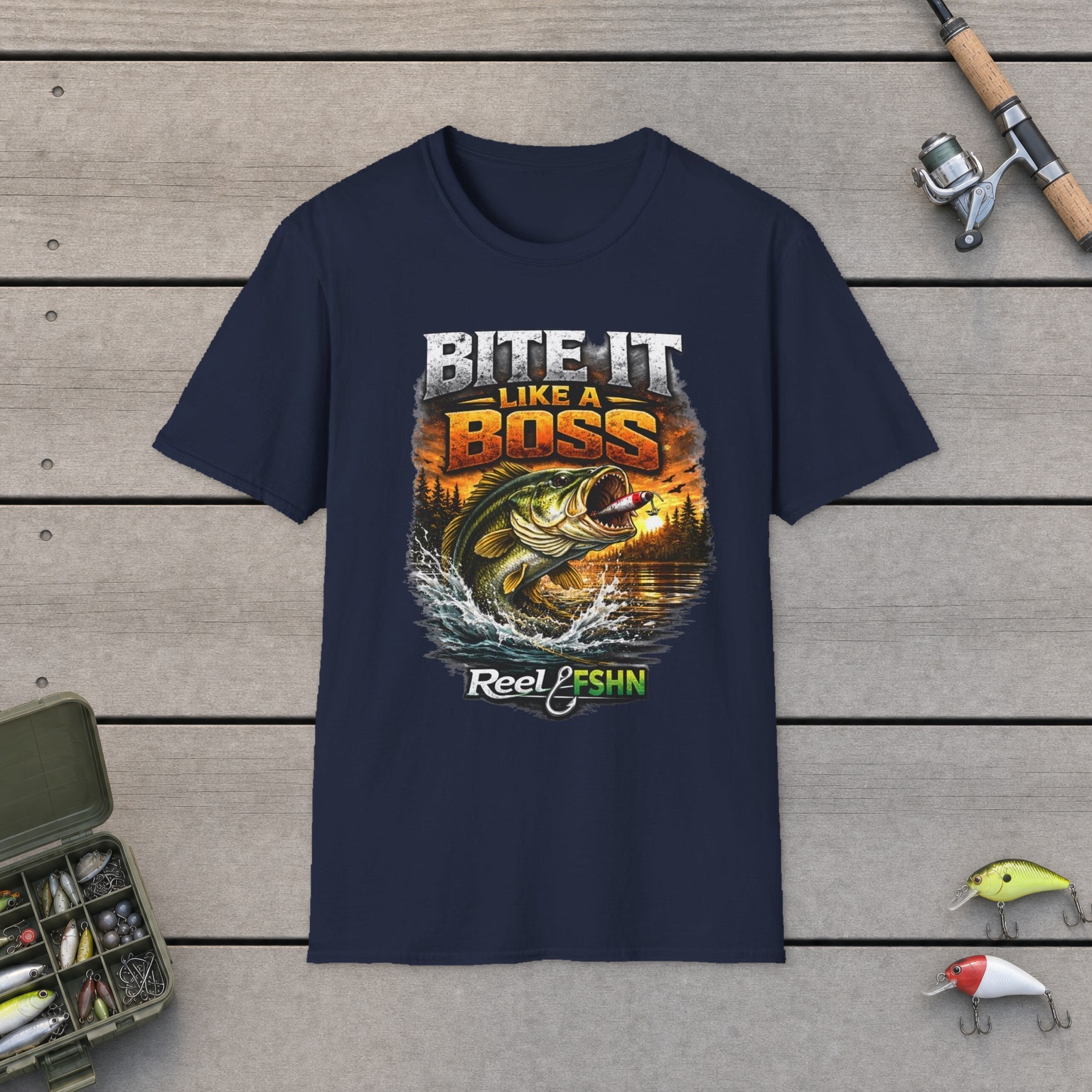 Bite It Like A Boss T-Shirt on a wooden dock with a fishing rod, reel, tackle box, and two lures