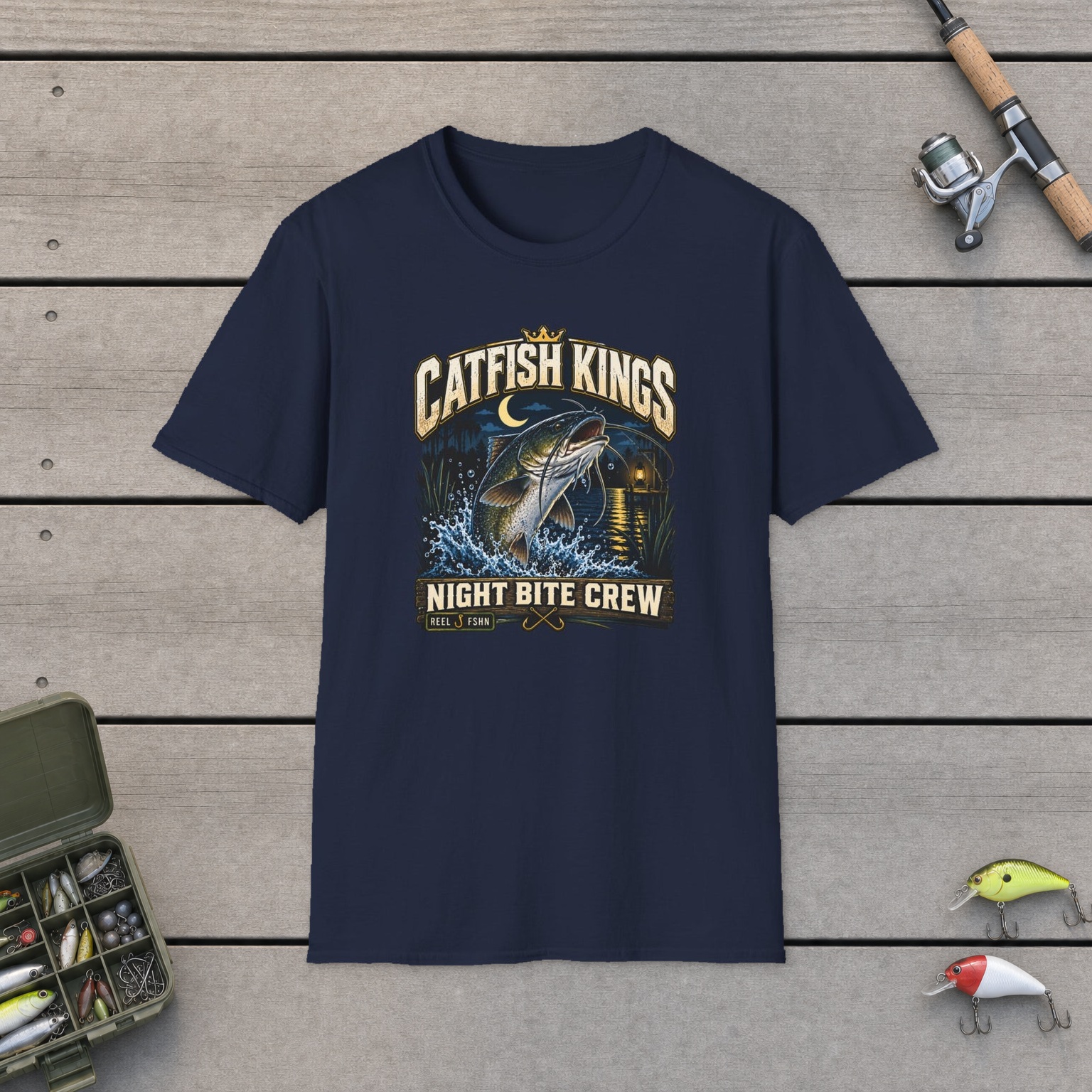 Catfish Kings T-Shirt on a wooden dock with a fishing rod, reel, tackle box, and two lures