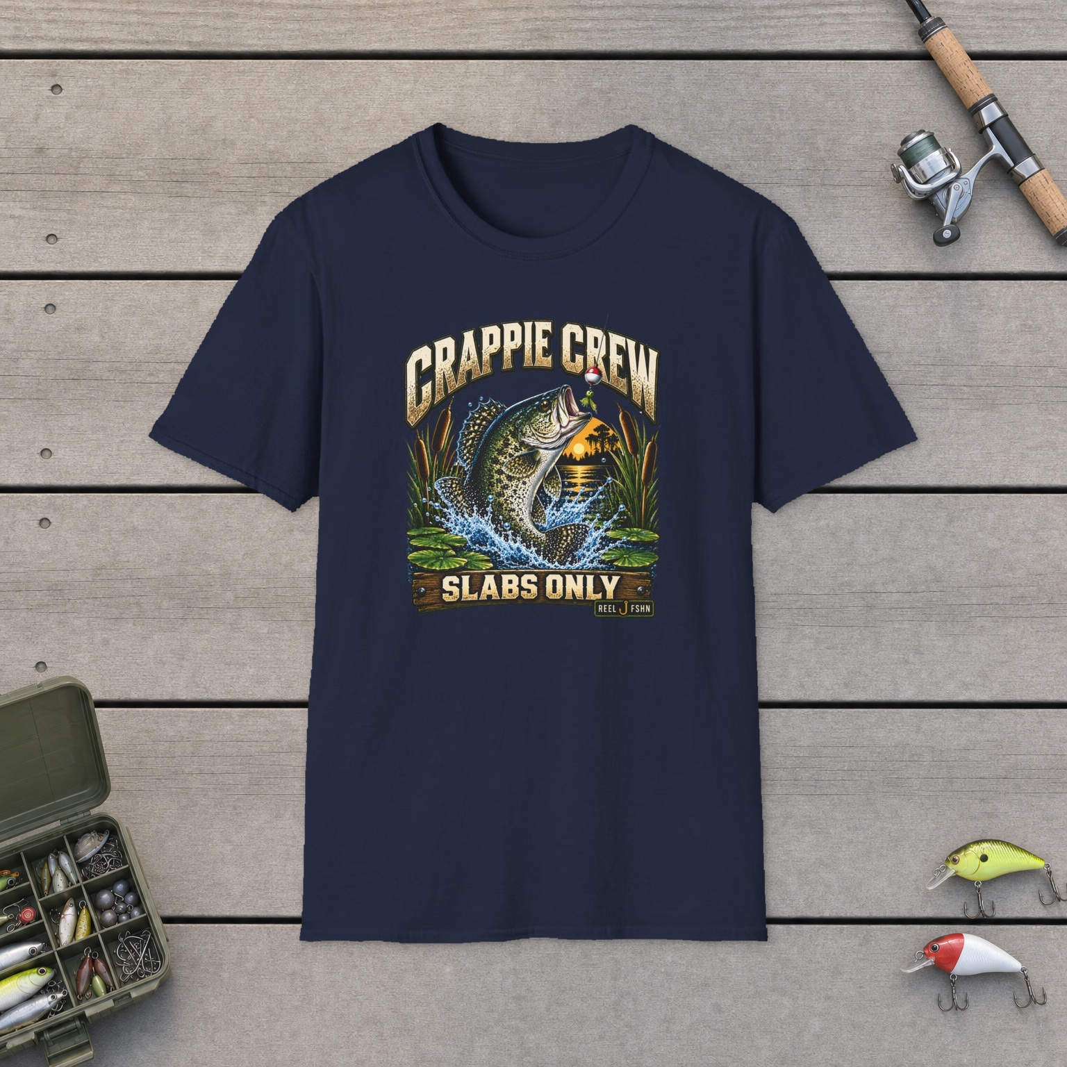 Crappie Crew T-Shirt on a wooden dock with a fishing rod, reel, tackle box, and two lures