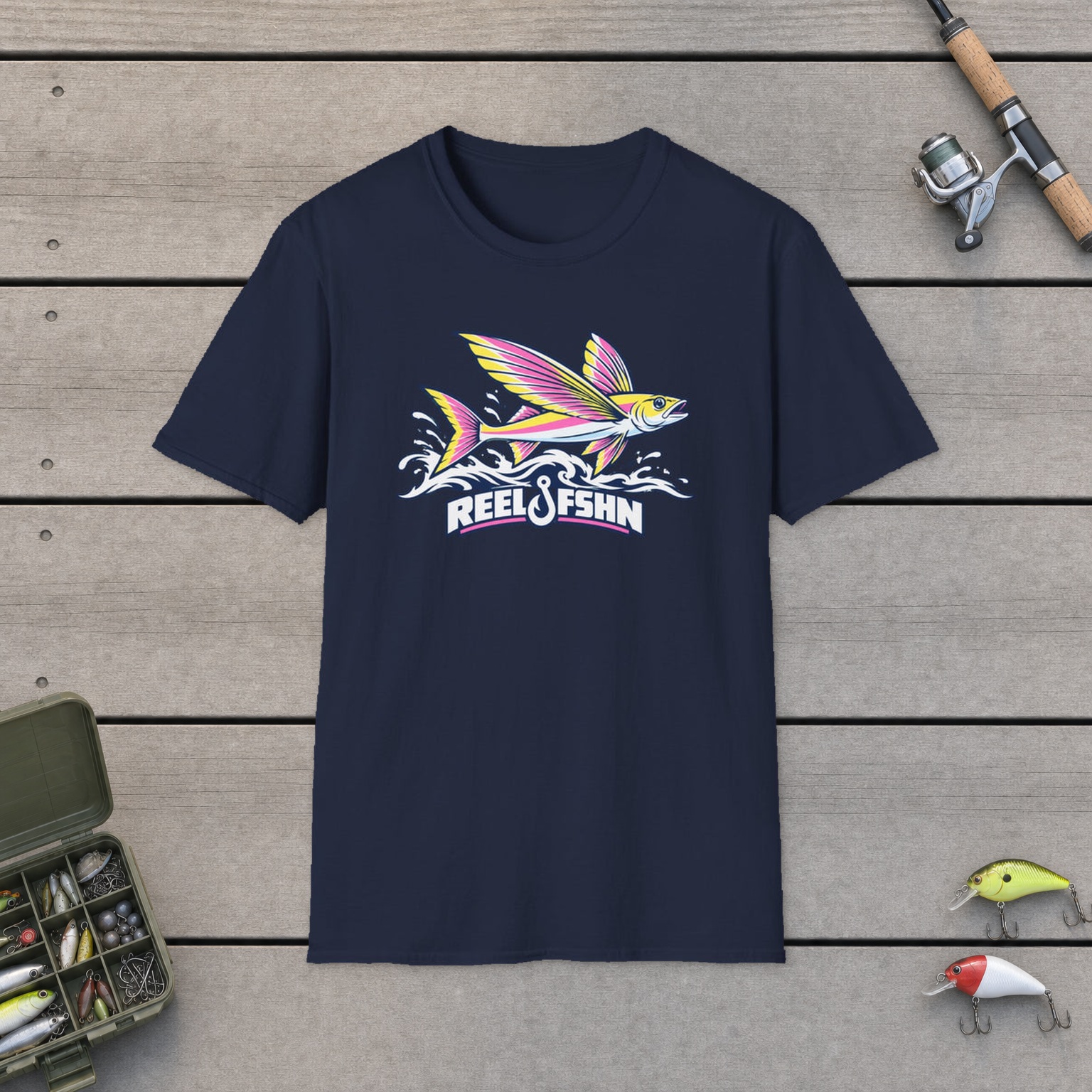 Flying Fish T-Shirt on a wooden dock with a fishing rod, reel, tackle box, and two lures