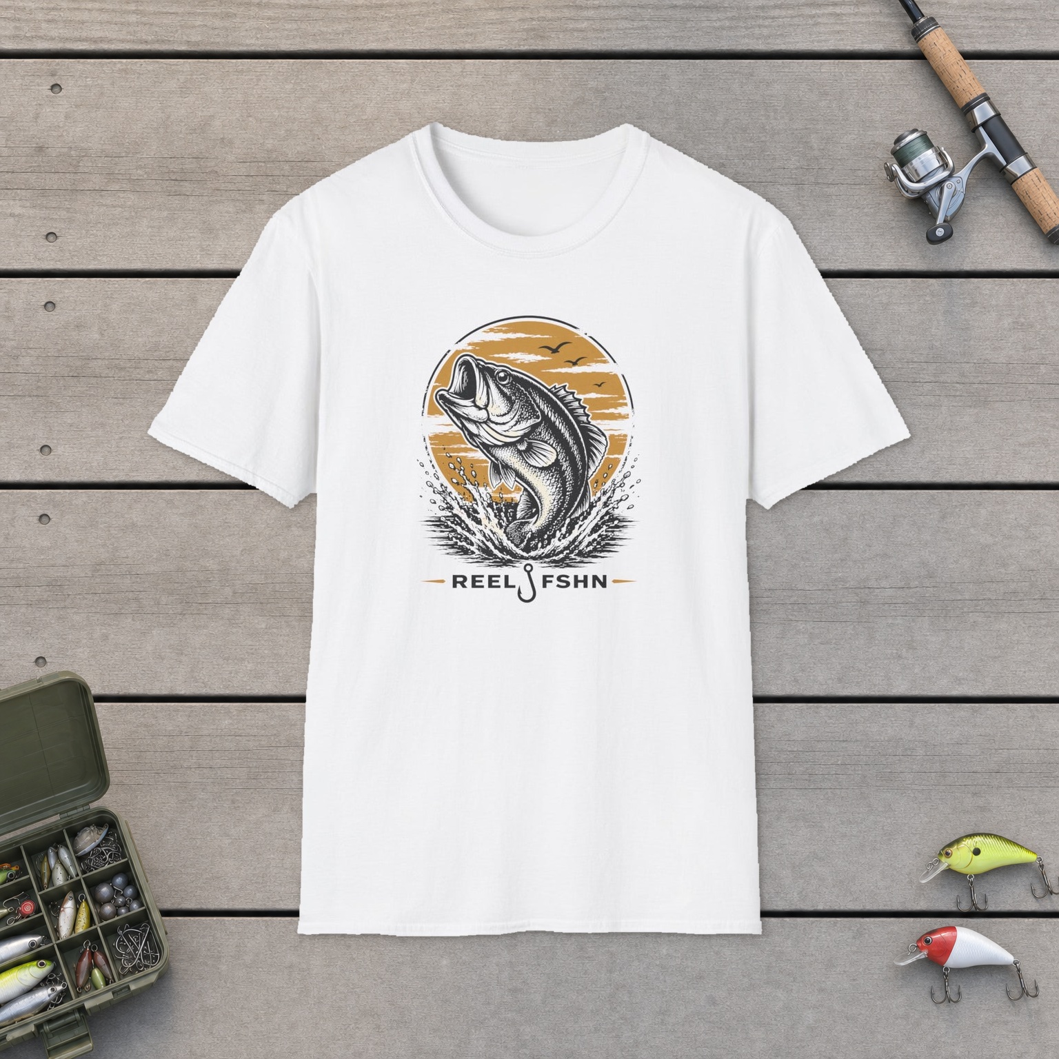 Jumping Bass T-Shirt on a wooden dock with a fishing rod, reel, tackle box, and two lures