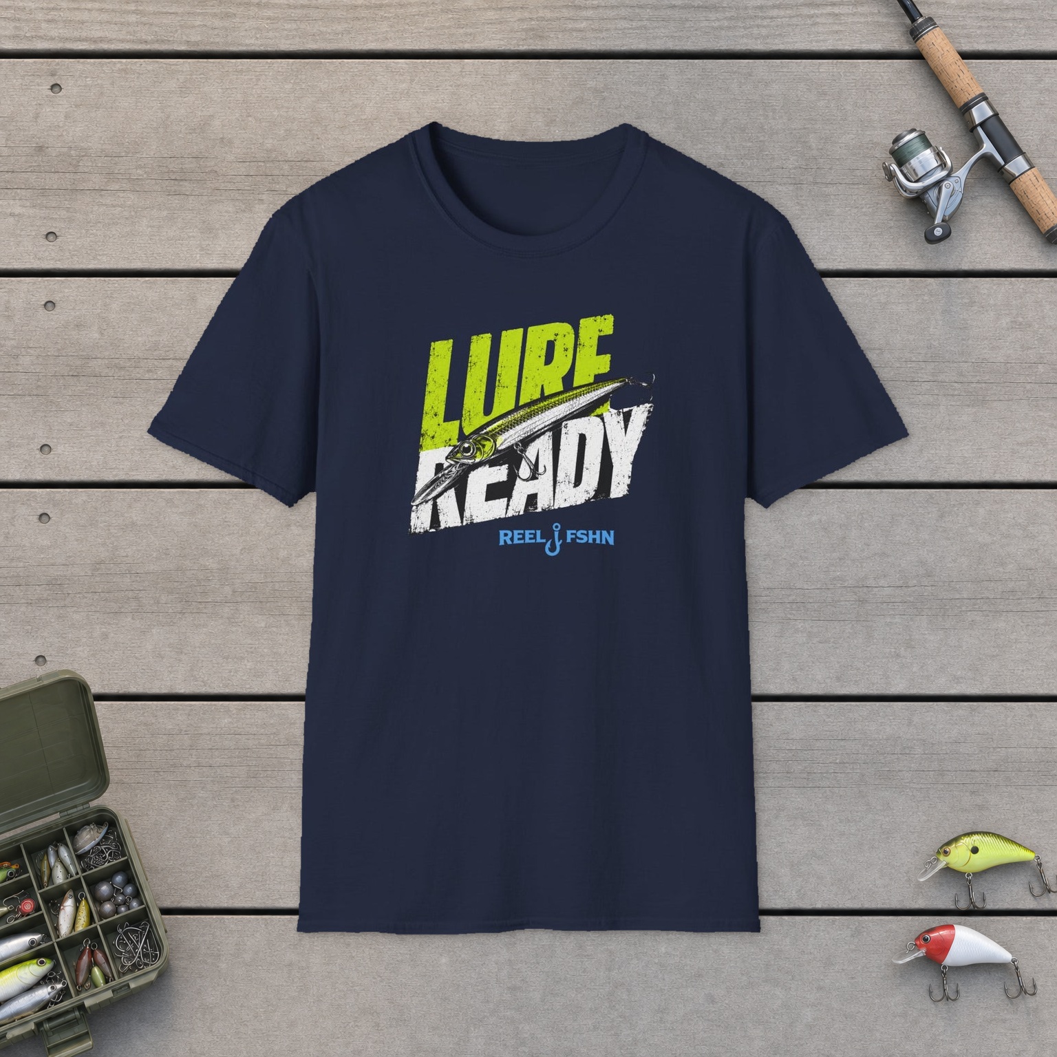 Lure Ready Slanted Logo T-Shirt on a wooden dock with a fishing rod, reel, tackle box, and two lures