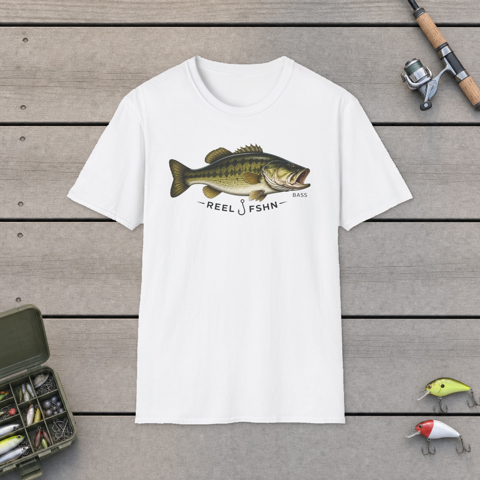 REEL FSHN BASS T-Shirt on a wooden dock with a fishing rod, reel, tackle box, and two lures
