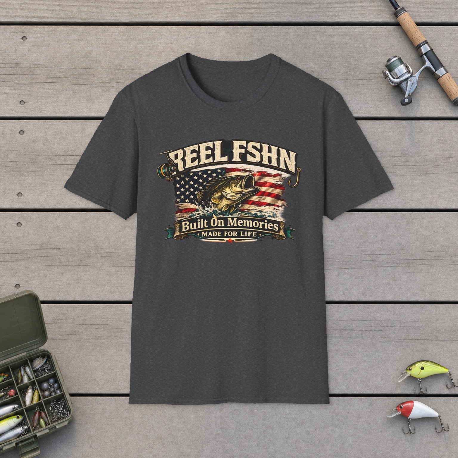 REEL FSHN Built On Memories T-Shirt on a wooden dock with a fishing rod, reel, tackle box, and two lures