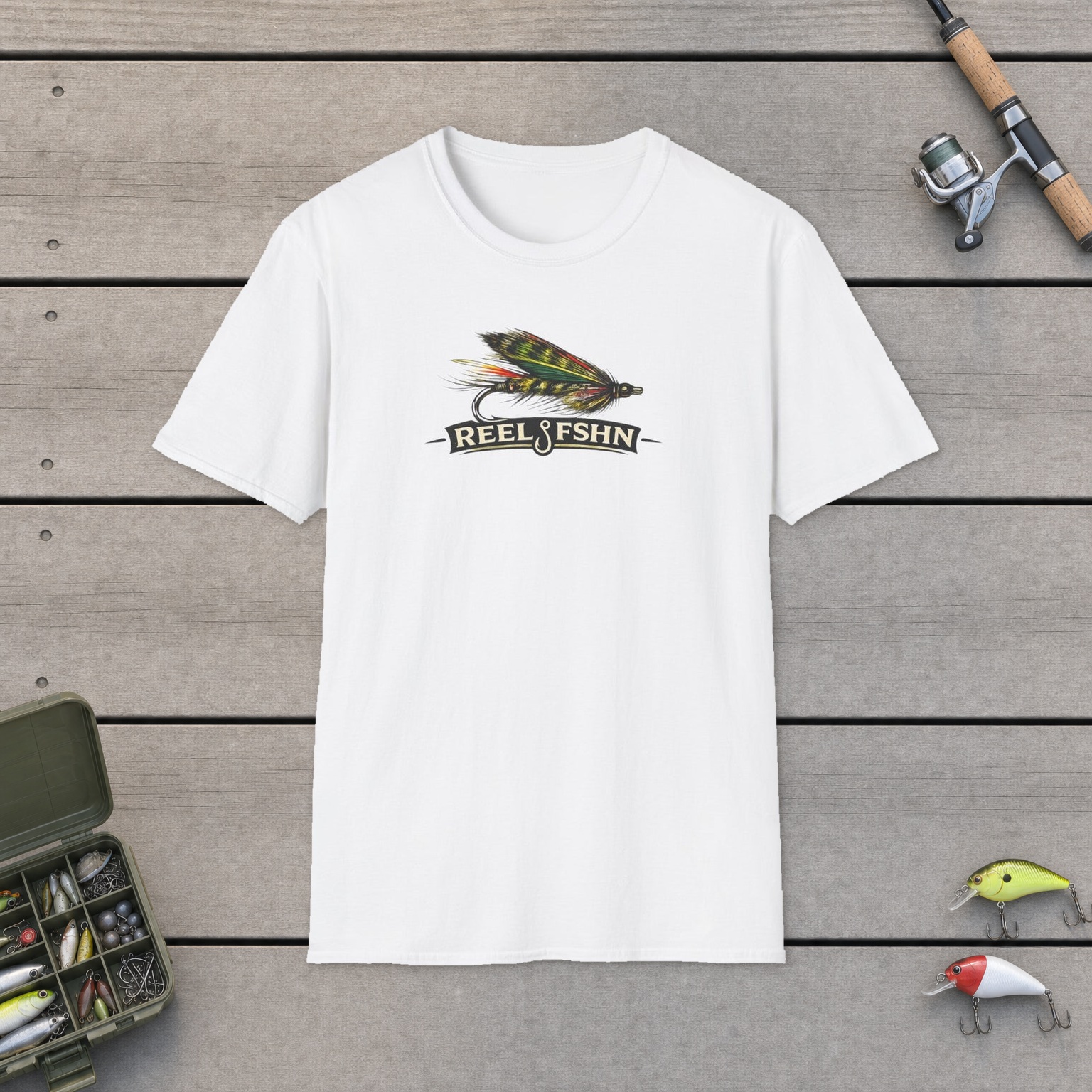 REEL FSHN FLY LURE T-Shirt on a wooden dock with a fishing rod, reel, tackle box, and two lures