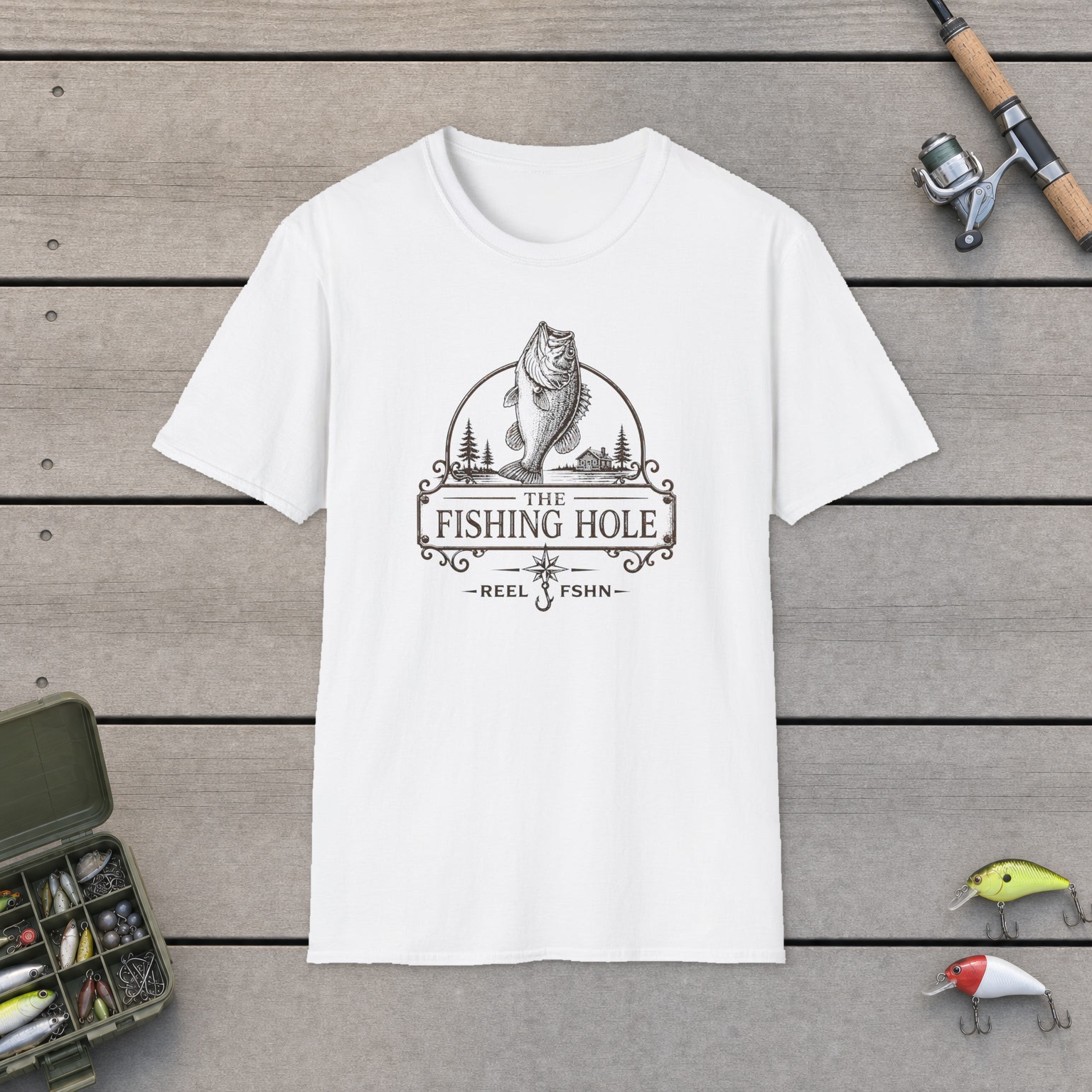 The Fishing Hole T-Shirt on a wooden dock with a fishing rod, reel, tackle box, and two lures