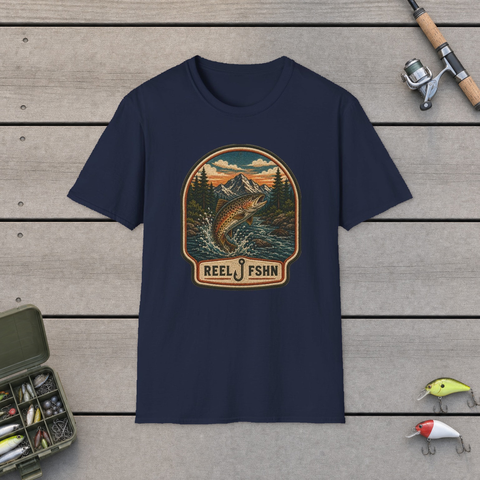 Trout Stream Patch T-Shirt on a wooden dock with a fishing rod, reel, tackle box, and two lures