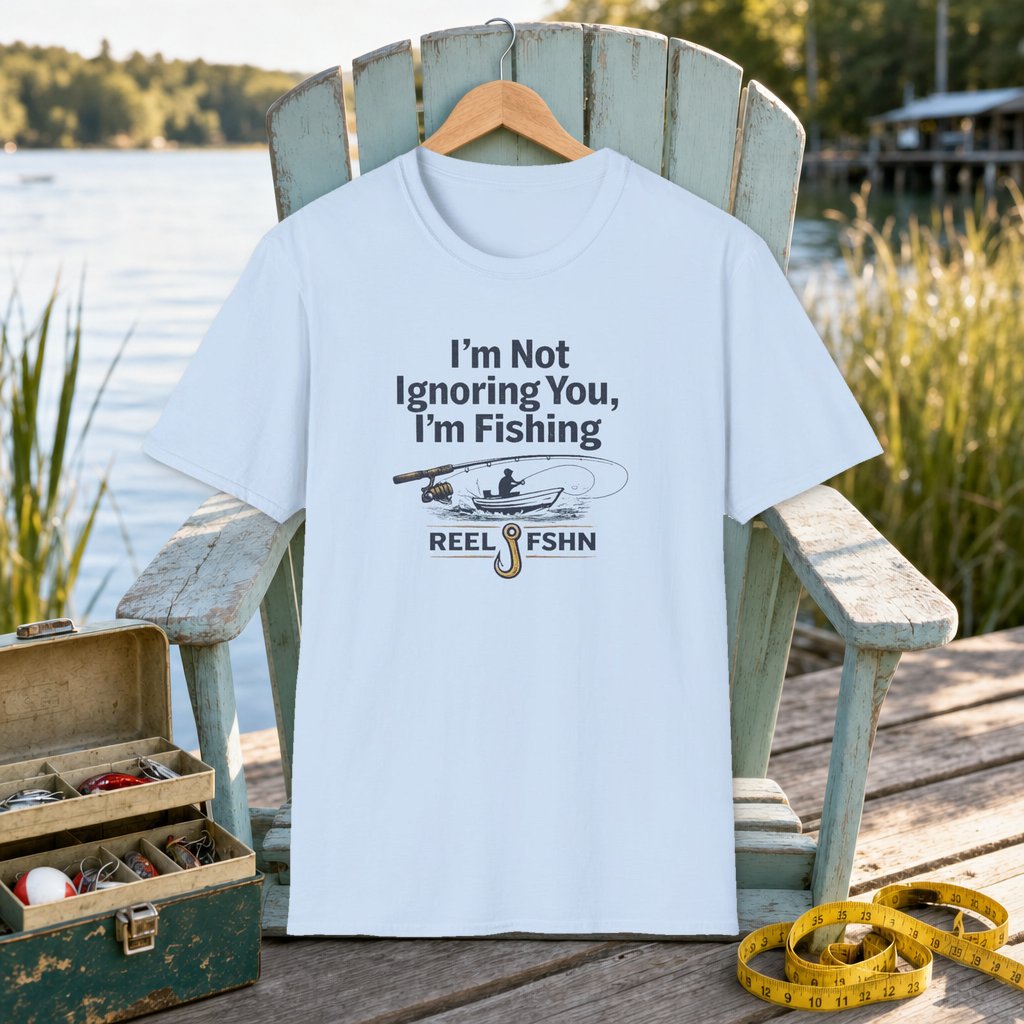 I'm Not Ignoring You, I'm Fishing T-Shirt on a hanger on a seafoam fishing chair beside a lake, tackle box, and measuring tape