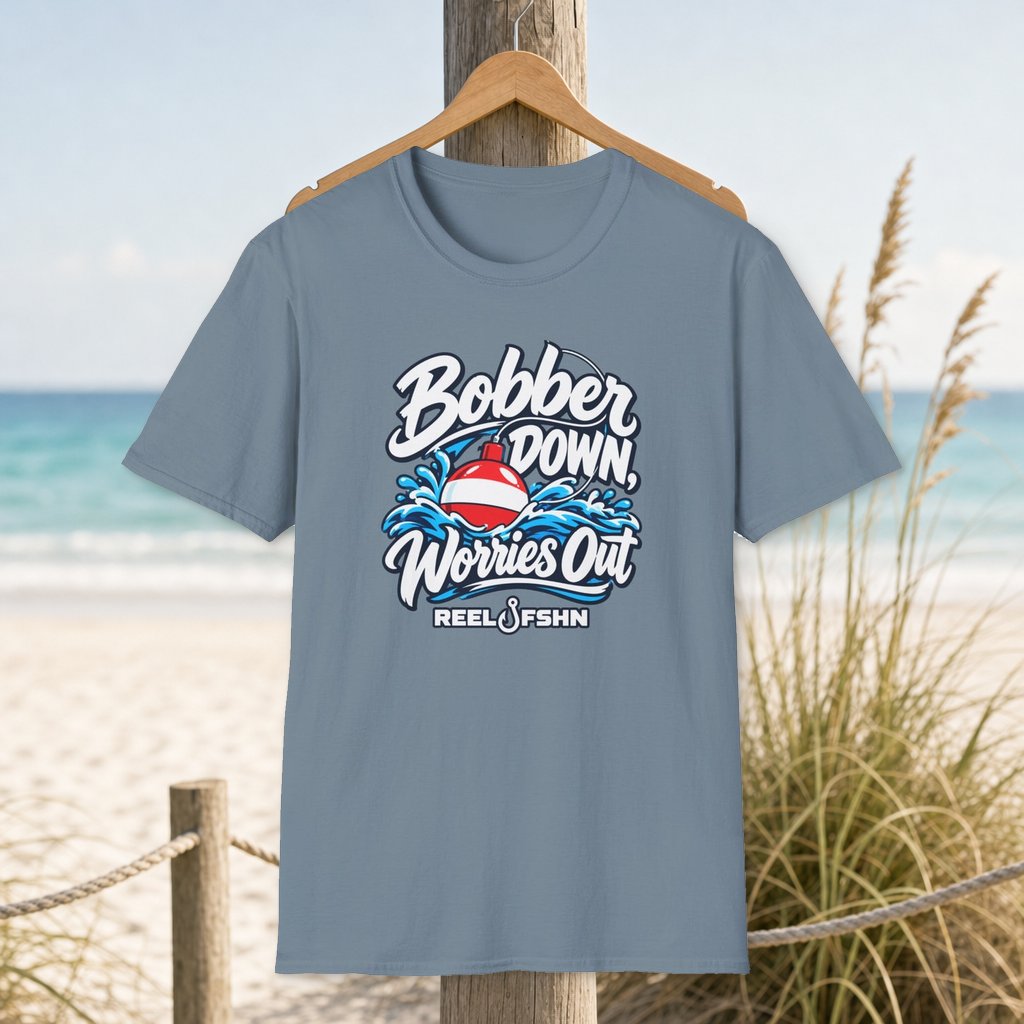 Bobber Down Worries Out T-Shirt on a hanger beside a sandy beach and turquoise coastal water
