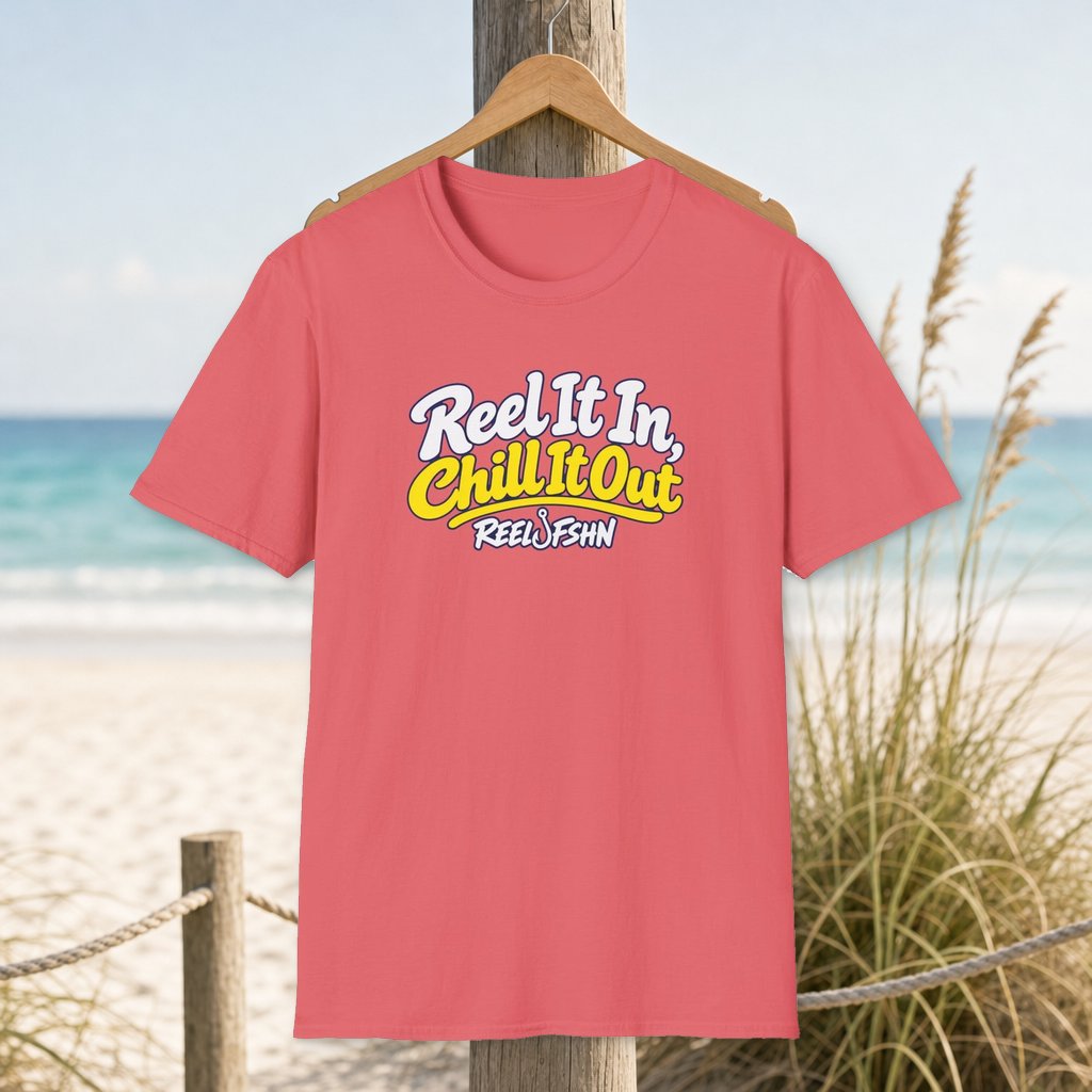 REEL It In, CHILL It Out T-Shirt on a hanger beside a sandy beach and turquoise coastal water