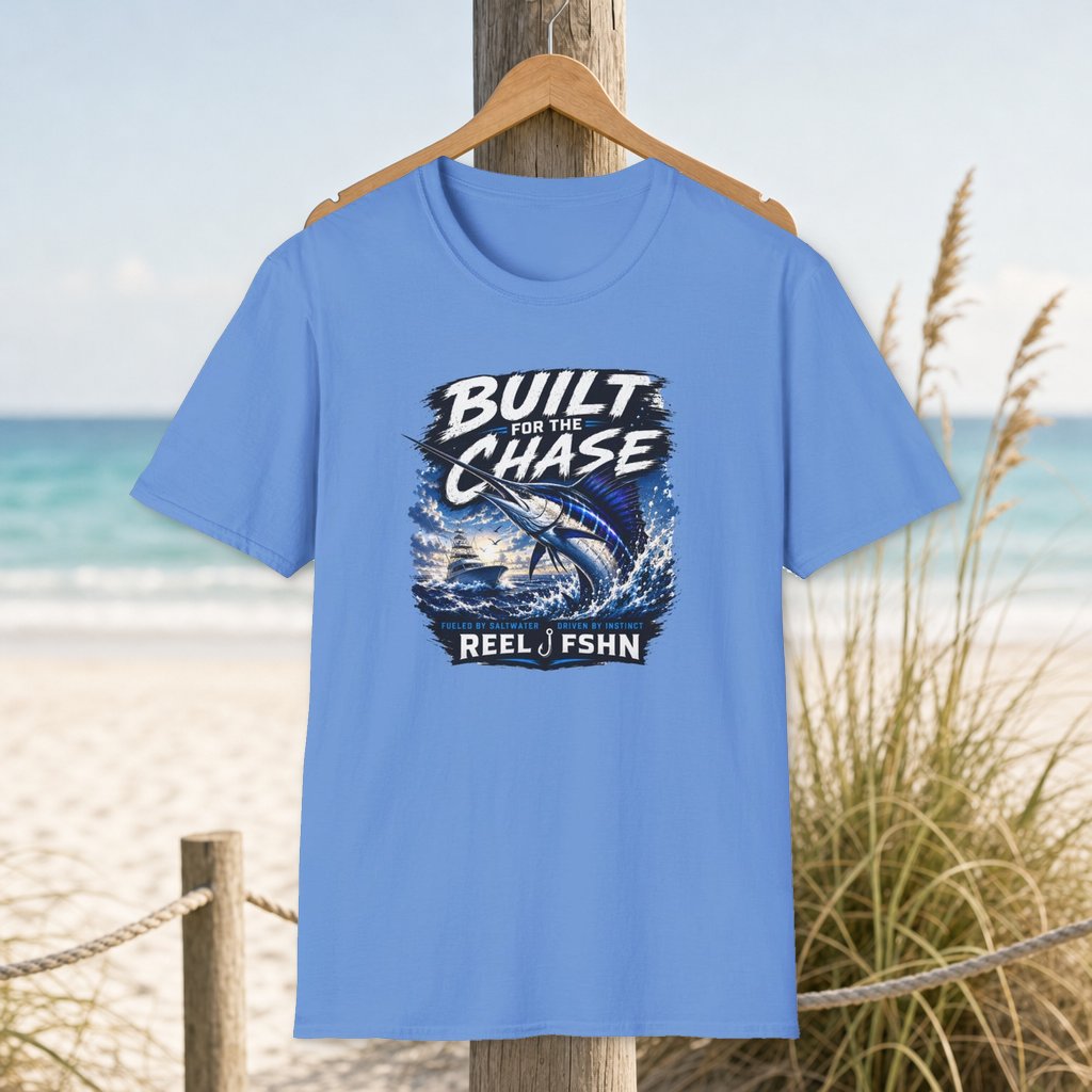 Built For The Chase Marlin T-Shirt on a hanger beside a sandy beach and turquoise coastal water