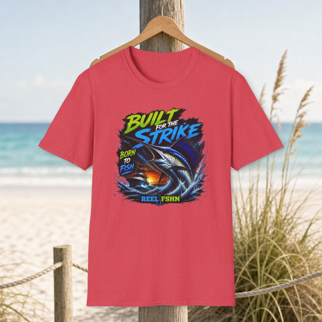 Built For The Strike Born To Fish T-Shirt on a hanger beside a sandy beach and turquoise coastal water