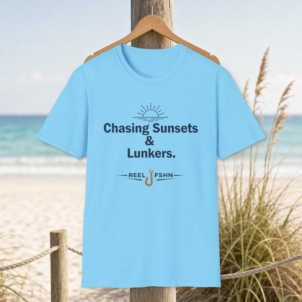 Chasing Sunsets & Lunkers T-Shirt on a hanger beside a sandy beach and turquoise coastal water