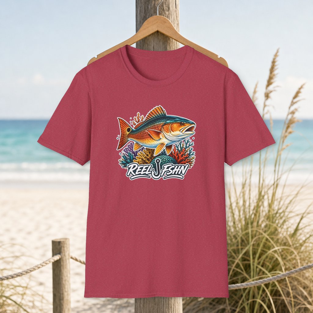 Coral Reef Redfish T-Shirt on a hanger beside a sandy beach and turquoise coastal water