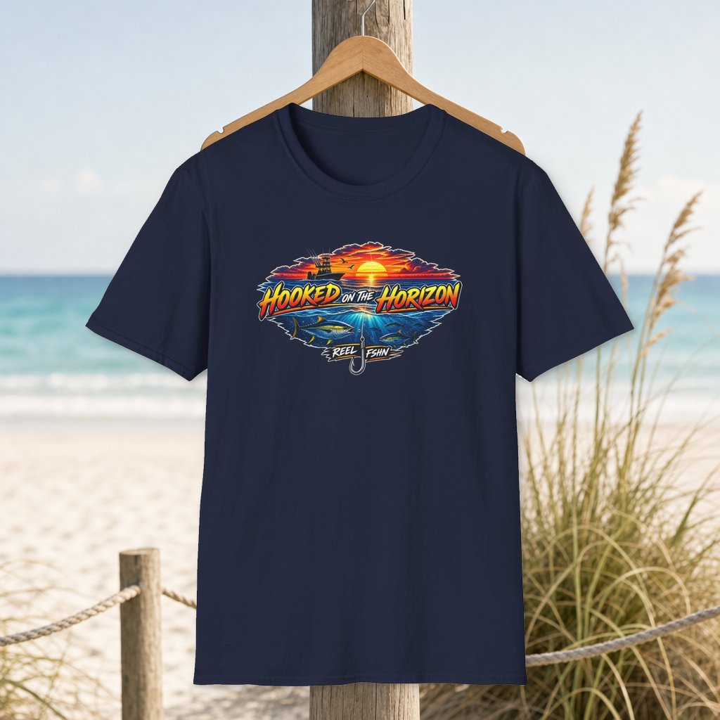 Hooked On The Horizon T-Shirt on a hanger beside a sandy beach and turquoise coastal water
