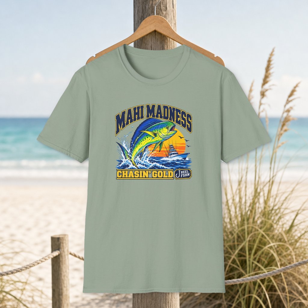 Mahi Madness T-Shirt on a hanger beside a sandy beach and turquoise coastal water