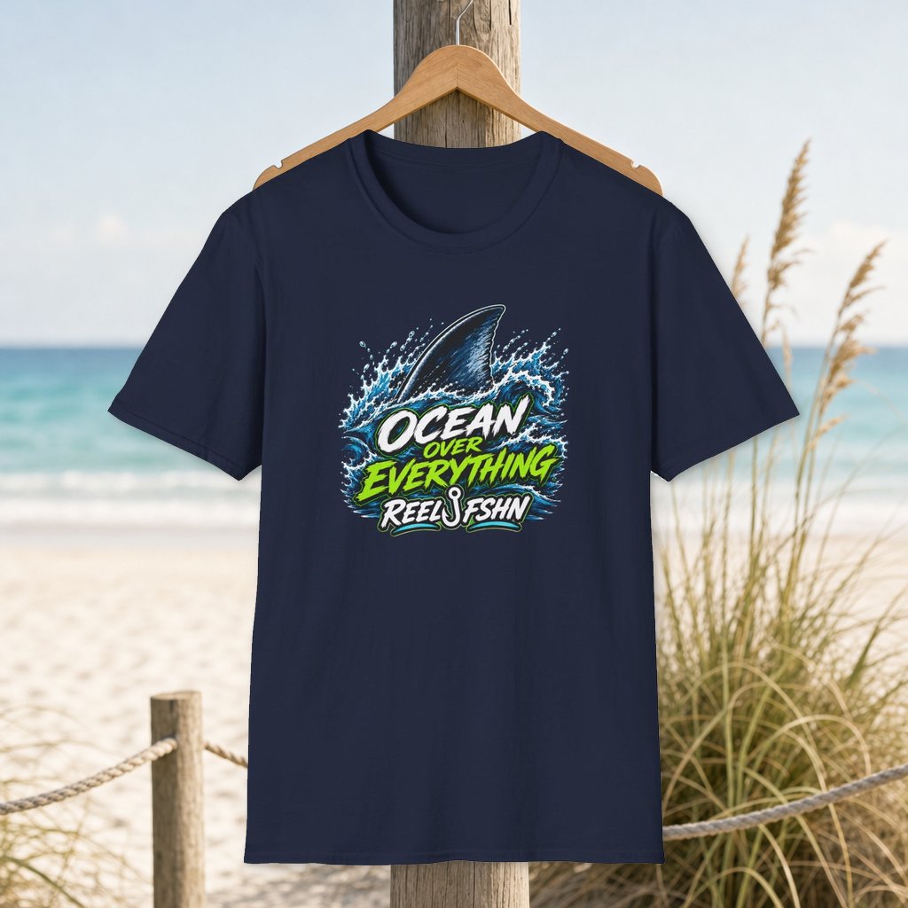 Ocean Over Everything T-Shirt on a hanger beside a sandy beach and turquoise coastal water