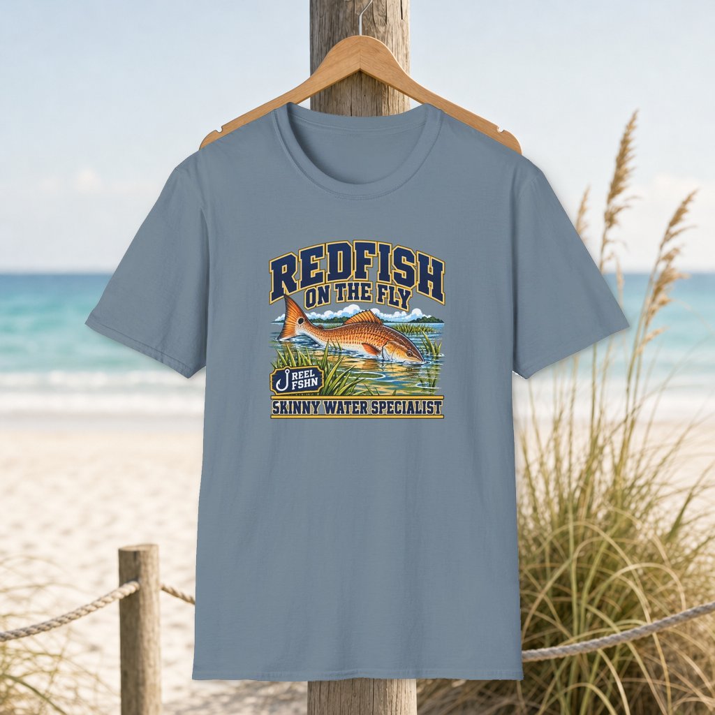 Redfish on the Fly T-Shirt on a hanger beside a sandy beach and turquoise coastal water