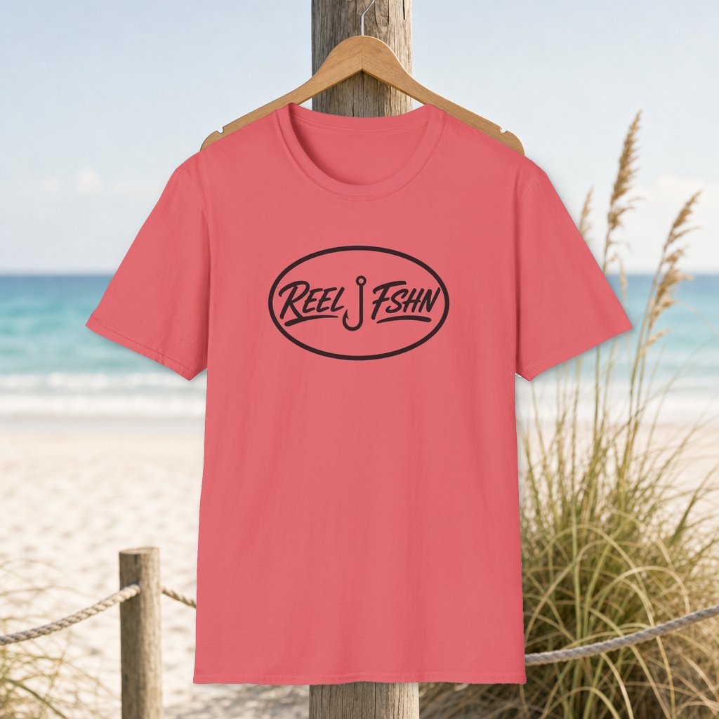 REEL FSHN Decal T-Shirt on a hanger beside a sandy beach and turquoise coastal water
