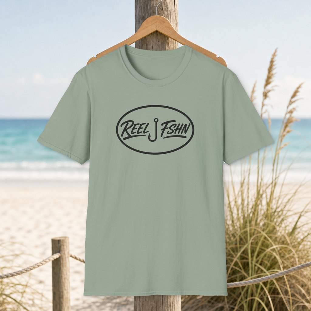 REEL FSHN Oval Badge T-Shirt on a hanger beside a sandy beach and turquoise coastal water