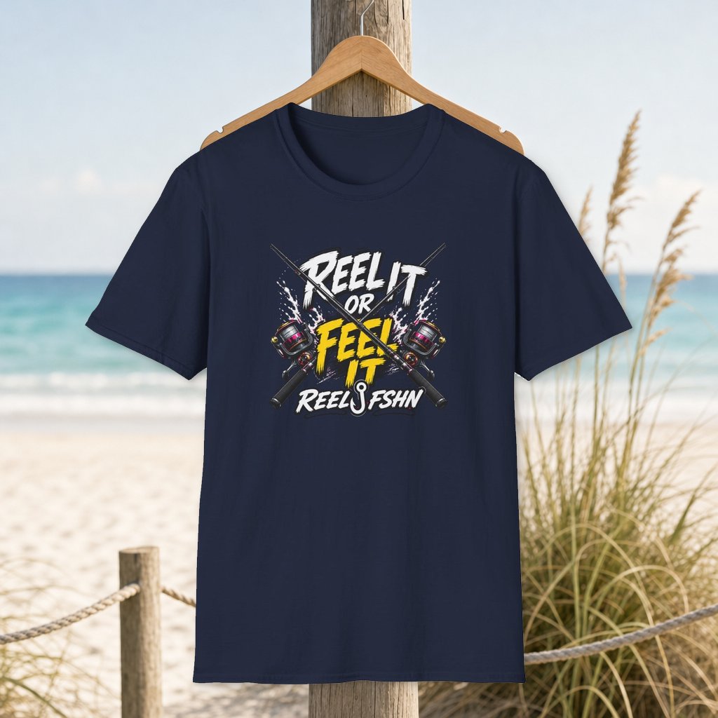 Reel It Or Feel It T-Shirt on a hanger beside a sandy beach and turquoise coastal water