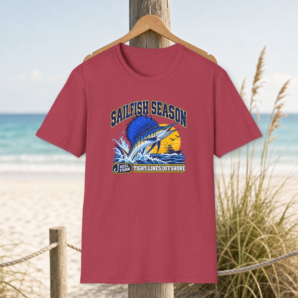 Sailfish Season T-Shirt on a hanger beside a sandy beach and turquoise coastal water