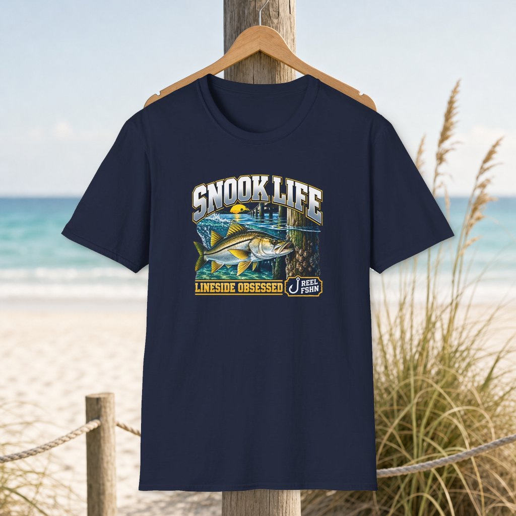 Snook Life T-Shirt on a hanger beside a sandy beach and turquoise coastal water