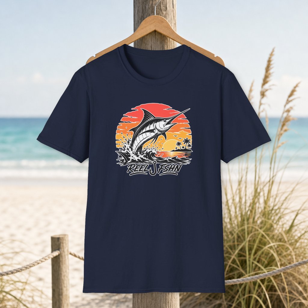 Sunset Marlin Run T-Shirt on a hanger beside a sandy beach and turquoise coastal water