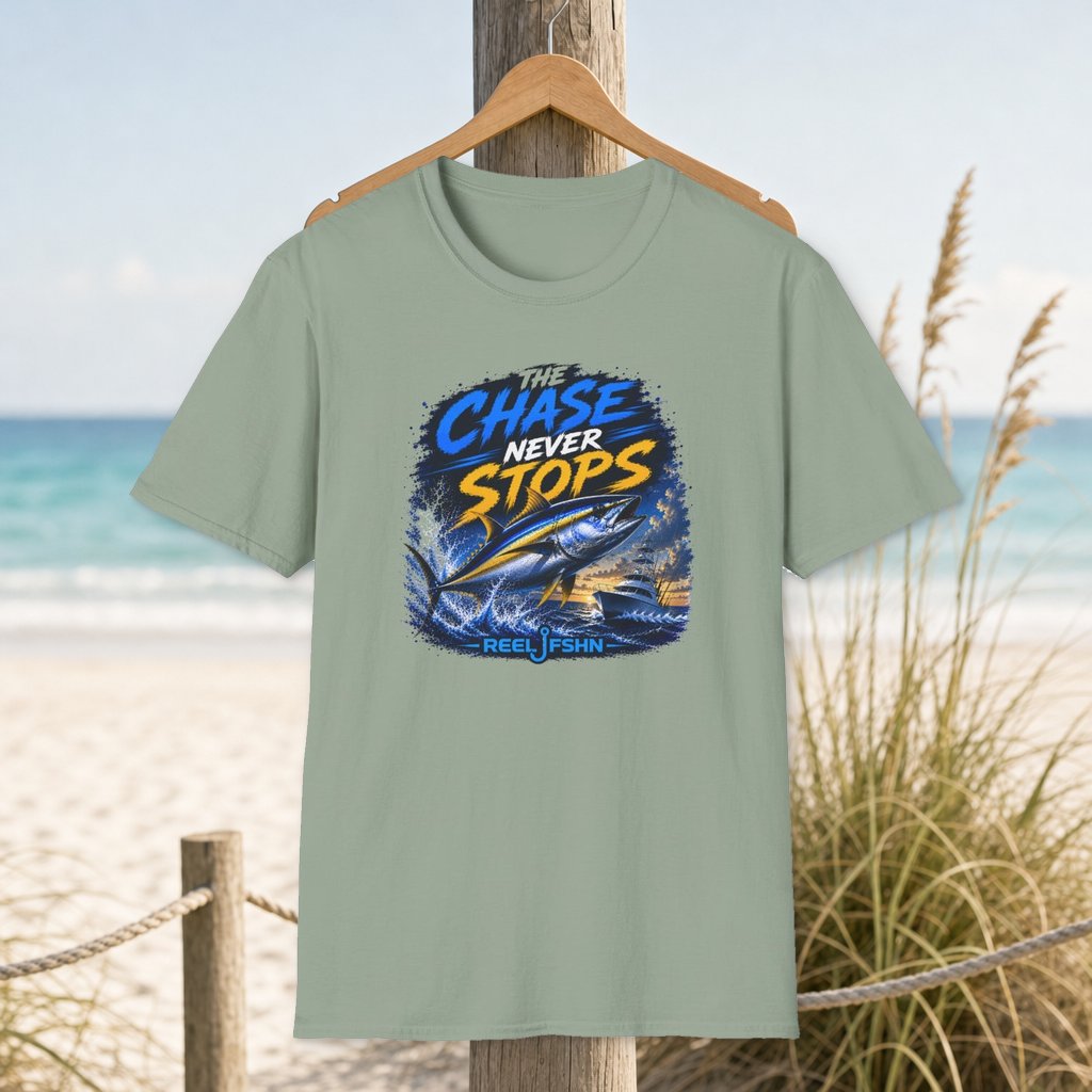 The Chase Never Stops T-Shirt on a hanger beside a sandy beach and turquoise coastal water