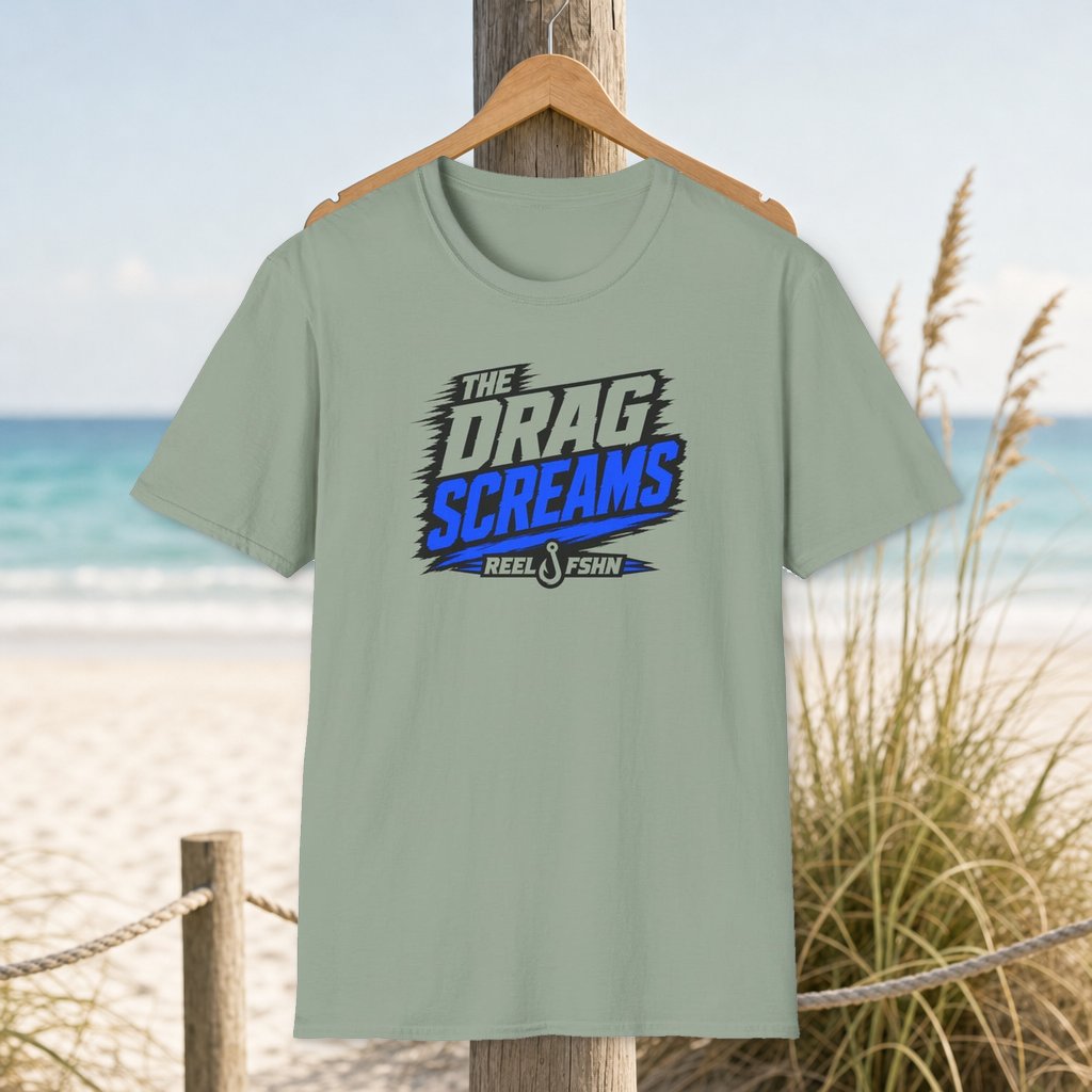The Drag Screams T-Shirt on a hanger beside a sandy beach and turquoise coastal water