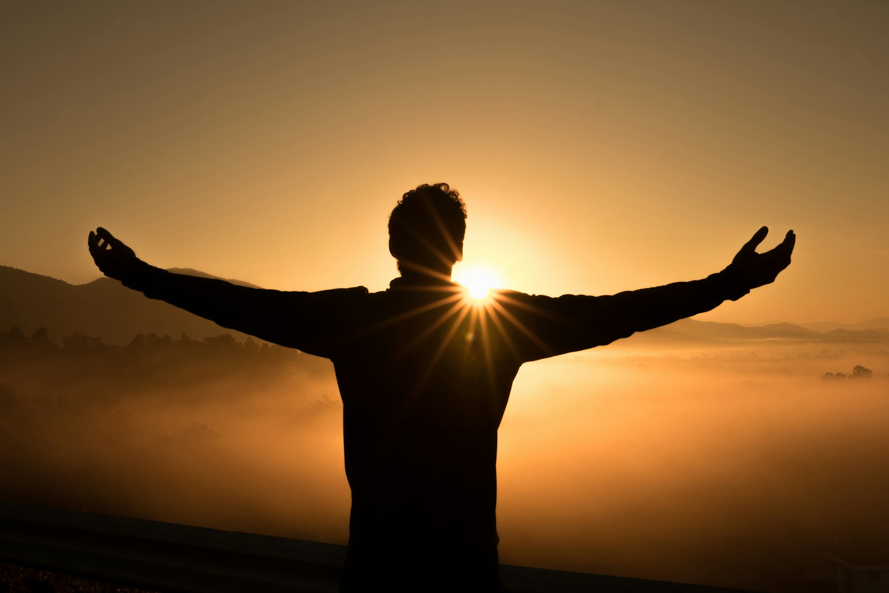 Person standing with arms open at sunrise