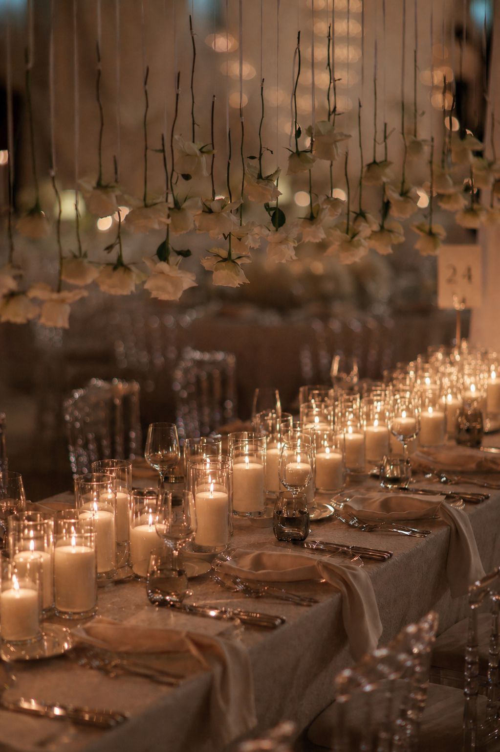 A long table illuminated by layered glass hurricanes beneath hanging white florals
